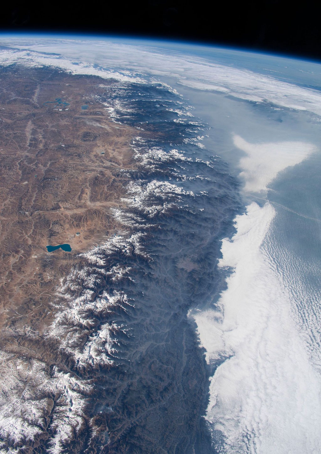 The expanse of the Himalayas rises above India to the right, covered in clouds, and the Tibetan plain to the left. Mt. Everest is near the middle, just to the left of center.