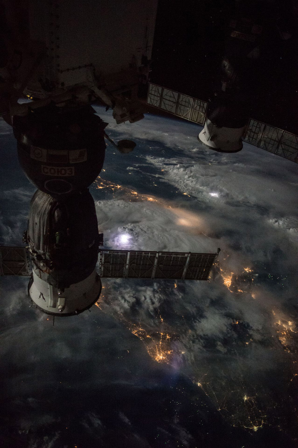 Image of two sattelites at the forefront looking at the surface of Earth with the bright lights of life