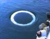 video still of people on a boat looking at w white ring on the ocean